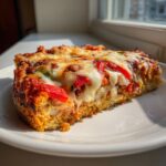 A thick slice of chicken crust pizza topped with red peppers and gooey, melted mozzarella cheese.