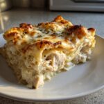 A close-up, appetizing slice of white chicken lasagna showing layers of pasta, shredded chicken, and a bubbly, browned cheese topping.