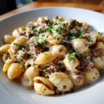 A close-up shot of creamy beef pasta made with shell-shaped pasta, topped with ground beef, cheese, and parsley.