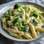 Close-up of creamy broccoli pasta made with penne, covered in a rich white sauce and topped with bright green broccoli florets.