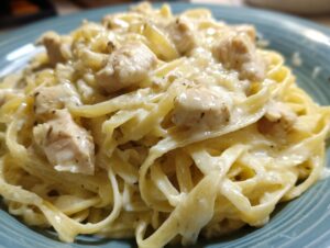 Close-up of fettuccine pasta smothered in creamy sauce with chunks of seasoned chicken, a perfect chicken alfredo dish.