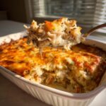 A spoonful of creamy chicken and wild rice casserole lifted from a baking dish with a golden, cheesy crust.