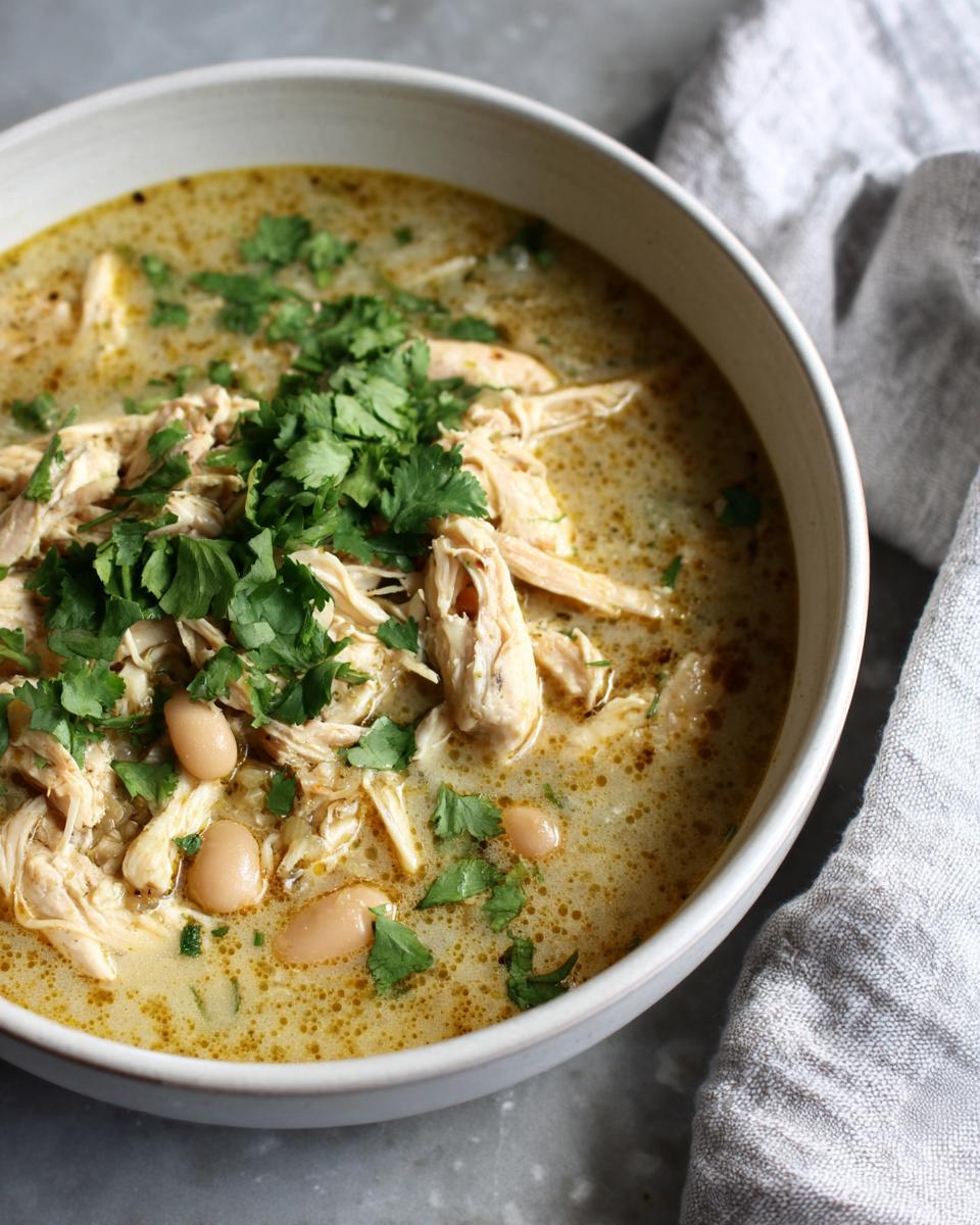 Close-up of a bowl of creamy white chicken chili featuring shredded chicken, white beans, and fresh cilantro garnish.