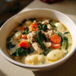 A close-up of a hearty bowl of creamy chicken and gnocchi soup with carrots and spinach.