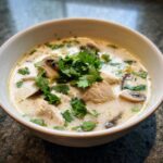 Close-up of a creamy chicken and mushroom coconut soup garnished generously with fresh cilantro.