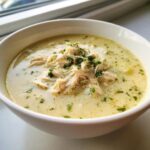 A close-up of creamy chicken poblano soup topped with shredded chicken and fresh parsley in a white bowl.
