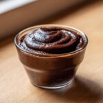 A close-up of thick, dark chocolate pudding swirled in a small glass dish.