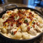 Close-up of creamy crack chicken gnocchi topped with bacon bits and cheese in a dark skillet.