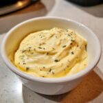 Close-up of thick, creamy homemade garlic aioli speckled with green herbs in a small white dipping bowl.