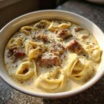 Close-up of a bowl of creamy italian sausage tortellini soup, topped with herbs and cheese.