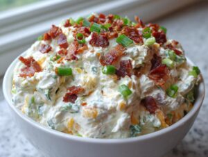 A close-up of a creamy Million Dollar Dip topped generously with crispy bacon bits and fresh green onions.