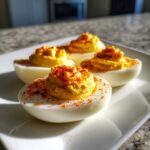 Four creamy deviled eggs piped high with filling and sprinkled with paprika on a white plate.