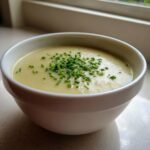 A close-up of a white bowl filled with creamy potato leek soup, topped generously with fresh chopped chives.
