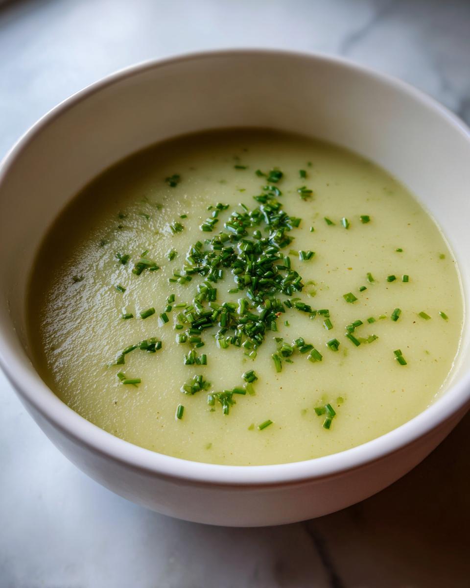 A close-up of creamy potato leek soup in a white bowl, garnished generously with chopped fresh chives.