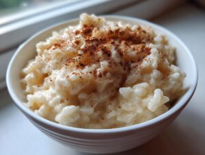 Close-up of a white bowl filled with creamy rice pudding topped generously with ground cinnamon.