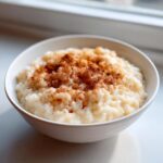 A close-up of creamy rice pudding topped generously with ground cinnamon in a white bowl.