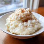 A close-up of creamy, white rice pudding recipe served in a white bowl and dusted generously with ground cinnamon.