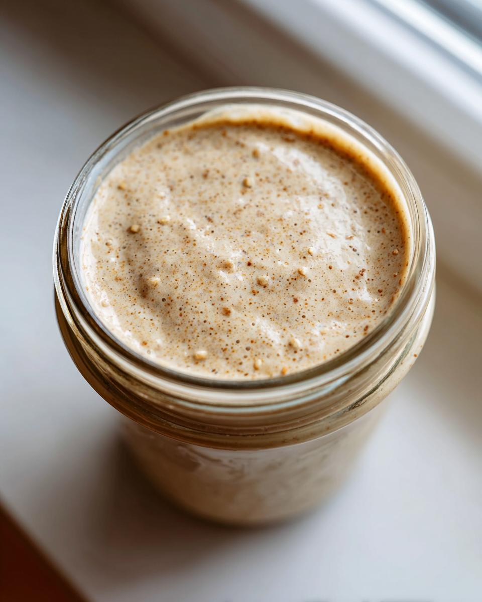 Overhead view of a creamy, speckled salad dressing blended smooth inside a clear glass jar.