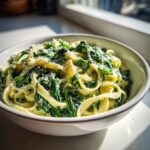 Close-up of creamy spinach pasta tossed with fettuccine noodles and topped with grated cheese.
