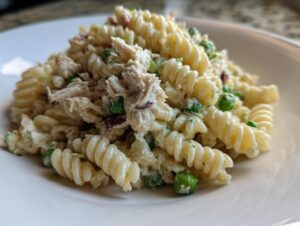 A close-up of a serving of creamy tuna pasta salad made with fusilli pasta, tuna flakes, and green peas.