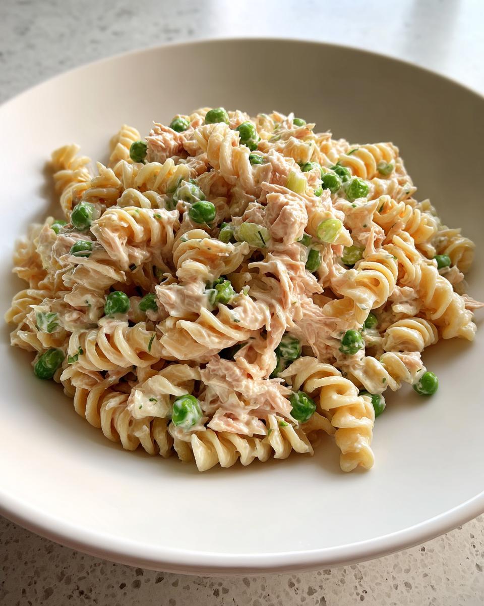 Close-up of creamy Tuna Pasta Salad mixed with rotini pasta, flaked tuna, and bright green peas, served in a white bowl.