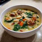 A close-up of a creamy white bean soup bowl filled with cannellini beans, meatballs, carrots, and spinach.