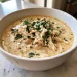 A close-up of creamy white chicken chili topped with shredded chicken, white beans, and fresh cilantro.