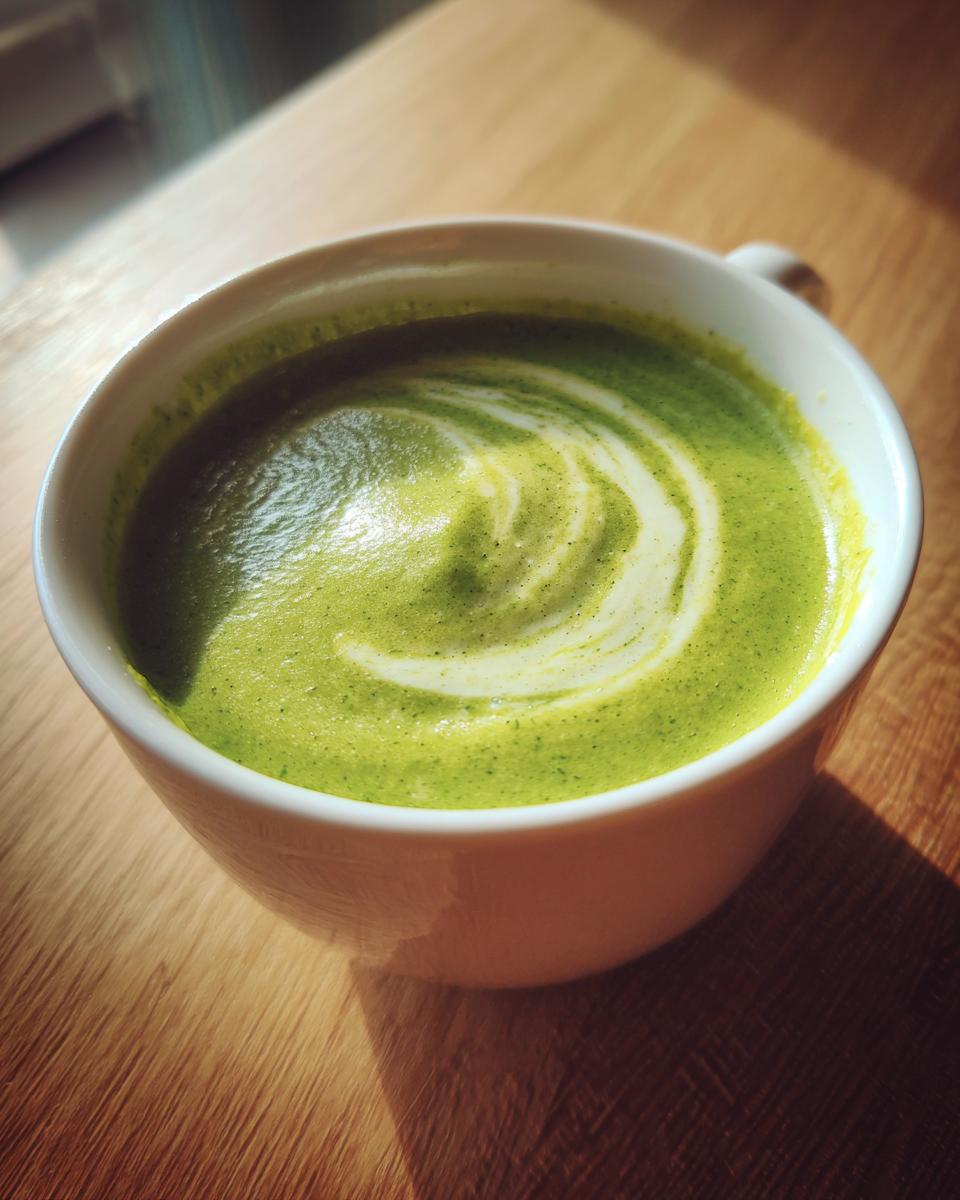 Close-up of creamy zucchini soup in a white mug, featuring a swirl of cream on top.
