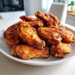 A close-up of a mound of golden brown, crispy air fryer chicken wings piled high on a white plate.