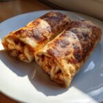 Two golden-brown, crispy Baked Chicken Chimichangas resting on a white plate, showing the shredded chicken filling.