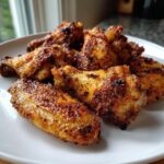 A close-up of several golden brown, seasoned crispy baked chicken wings piled on a white plate.