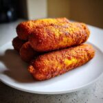 A stack of four perfectly golden brown, crispy corn dogs piled on a white plate.