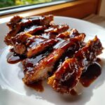 Close-up of crispy, sliced meat generously coated in thick, glossy homemade teriyaki sauce on a white plate.