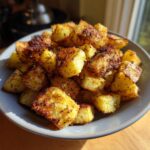 A close-up of golden brown, crispy oven roasted potatoes seasoned with herbs in a grey bowl.