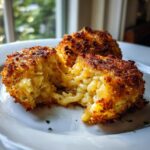 Close-up of crispy, golden-brown potato croquettes, one broken open revealing a creamy interior.
