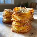 Close-up of golden brown, crispy potato stacks layered with melted cheese and herbs.