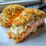 Two portions of baked stuffed salmon topped with creamy filling and a thick, golden, crispy breadcrumb crust.