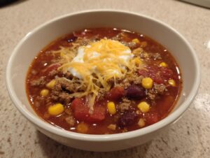 A close-up of a bowl of rich crockpot cowboy soup topped with sour cream and shredded cheddar cheese.