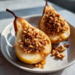 Two halves of sweet baked pears filled with a crunchy walnut crumble topping, served on a plate.