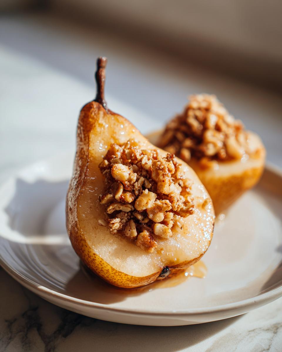Two halves of glistening baked pears, one in focus, filled with a crunchy nut and spice topping.