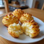Four golden-brown duchess potatoes piped into decorative swirls, one broken open to show the fluffy interior.