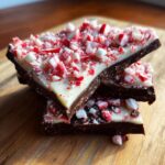 Three stacked pieces of dark and white chocolate peppermint bark recipe topped with crushed candy canes.