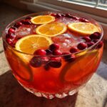 Close-up of a vibrant red thanksgiving punch garnished with fresh orange slices and whole cranberries.