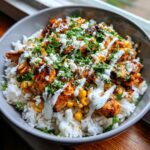 Close-up of a delicious chicken rice bowl featuring seasoned chicken, white rice, corn, white sauce drizzle, and cilantro.