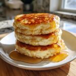 A tall stack of three fluffy almond flour pancakes drizzled generously with golden syrup.