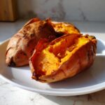 Two fluffy baked sweet potato halves showing bright orange flesh on a white plate.
