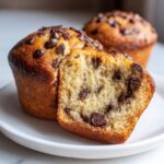 Close-up of a fluffy banana chocolate chip muffin cut in half showing the moist interior and melted chocolate chips.