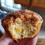 A hand holds a partially eaten french toast muffin showing its soft, airy interior and cinnamon sugar topping.