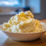 A generous serving of creamy, fluffy mashed potatoes topped with melted butter in a white bowl.