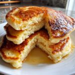 Close-up of a stack of fluffy pancakes cut open, showing the airy interior and drizzled with golden syrup.